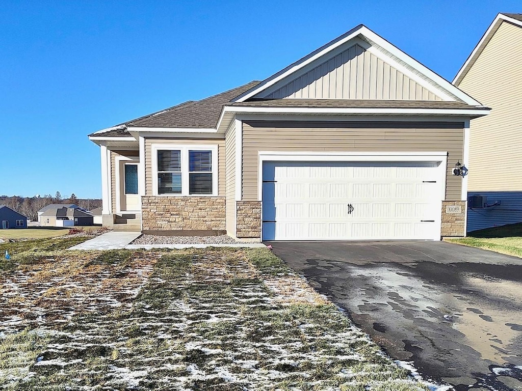 view of front of property featuring stone siding, board and batten siding, an attached garage, and driveway