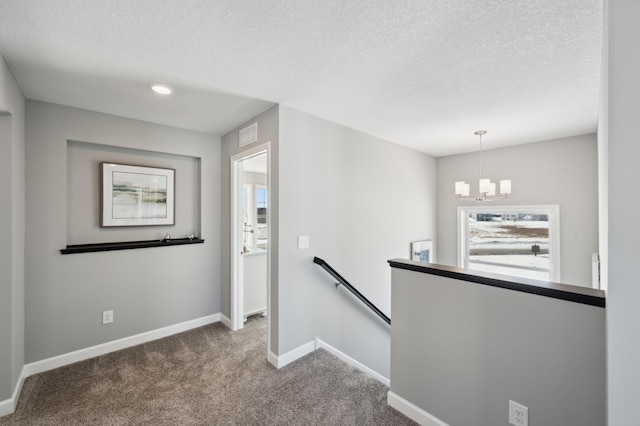 corridor with baseboards, an upstairs landing, an inviting chandelier, a textured ceiling, and carpet flooring