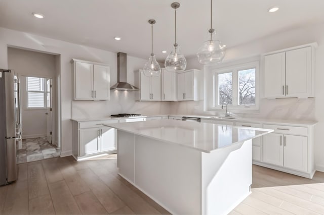 kitchen with wall chimney range hood, a wealth of natural light, stainless steel appliances, and light countertops