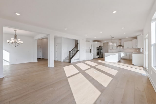 unfurnished living room with stairs, light wood-style floors, a chandelier, a sink, and recessed lighting