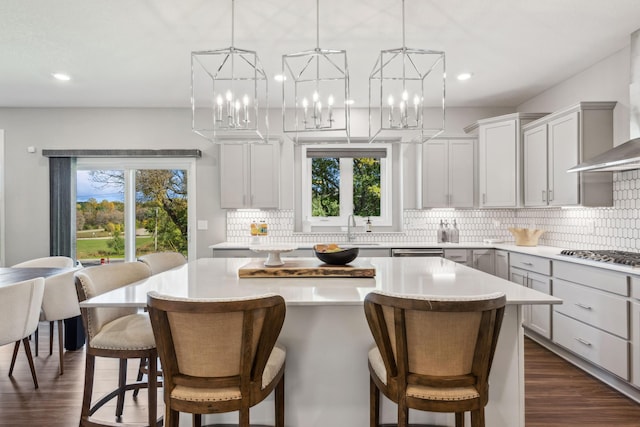 kitchen featuring a center island, tasteful backsplash, light countertops, stainless steel gas stovetop, and wall chimney exhaust hood