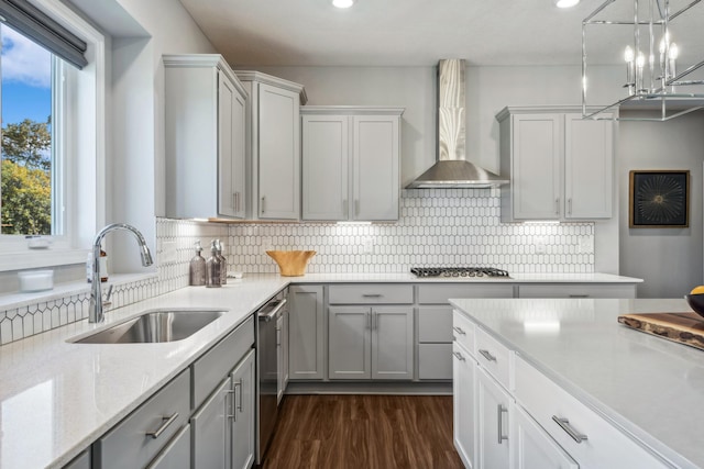 kitchen with tasteful backsplash, stainless steel appliances, gray cabinetry, wall chimney range hood, and a sink