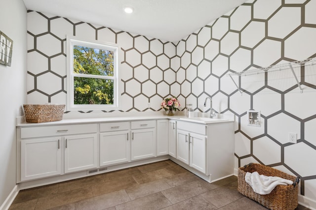 kitchen with light countertops, visible vents, backsplash, white cabinets, and a sink