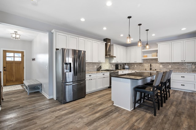 kitchen with dark countertops, appliances with stainless steel finishes, white cabinetry, a kitchen island, and wall chimney range hood