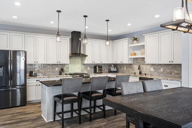 kitchen featuring wall chimney range hood, white cabinetry, stainless steel appliances, and a center island