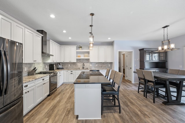 kitchen featuring a kitchen island, stainless steel gas range, freestanding refrigerator, wall chimney exhaust hood, and decorative light fixtures