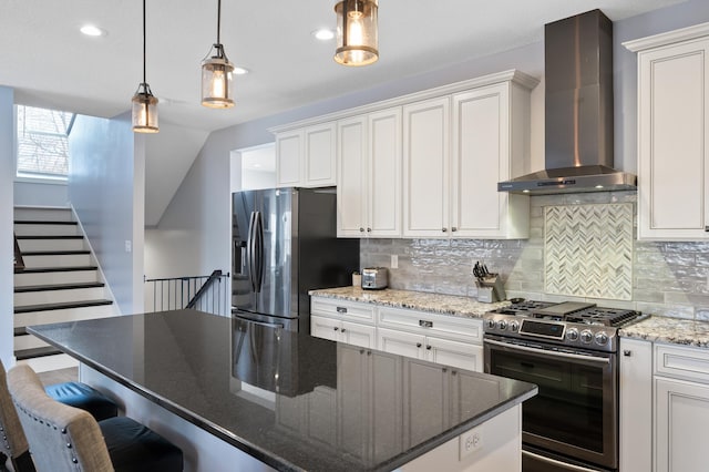 kitchen featuring a center island, black refrigerator with ice dispenser, wall chimney range hood, white cabinetry, and stainless steel range with gas stovetop