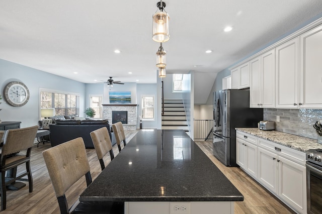 kitchen featuring a kitchen island, white cabinetry, open floor plan, dark stone countertops, and decorative light fixtures