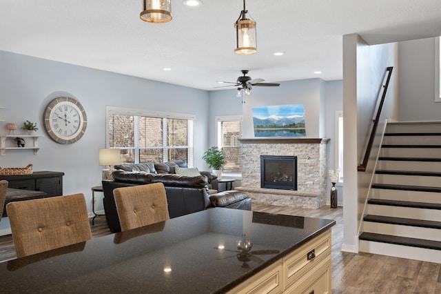 kitchen featuring a stone fireplace, light wood-style flooring, open floor plan, dark stone counters, and decorative light fixtures