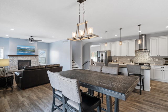 dining area with recessed lighting, stairway, dark wood-type flooring, and a stone fireplace