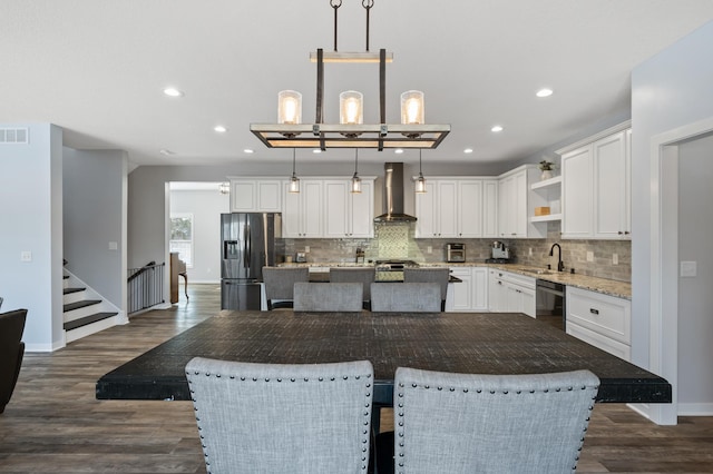 kitchen with pendant lighting, a kitchen island, wall chimney range hood, and stainless steel fridge with ice dispenser