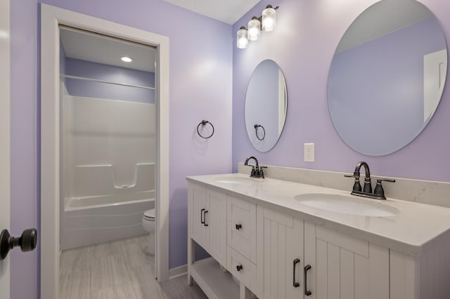 bathroom featuring double vanity, shower / bathing tub combination, a sink, and toilet