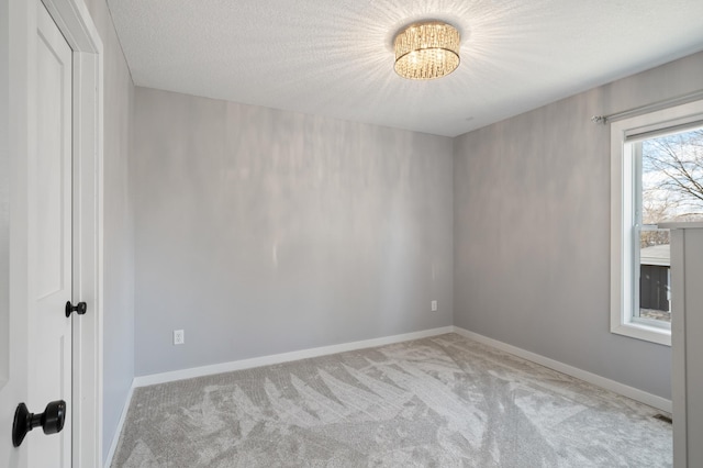 spare room featuring an inviting chandelier, baseboards, a textured ceiling, and light colored carpet