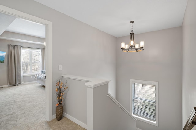 hall with carpet, baseboards, a chandelier, and an upstairs landing