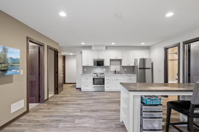 kitchen featuring visible vents, white cabinets, a sink, stainless steel appliances, and backsplash