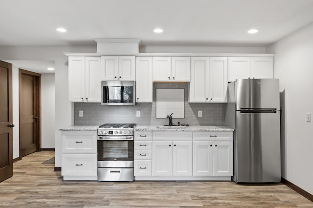 kitchen featuring light wood-style flooring, light stone counters, stainless steel appliances, white cabinetry, and a sink