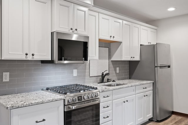 kitchen featuring white cabinets, light stone counters, stainless steel appliances, and a sink