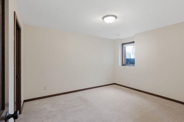 empty room with light carpet, a textured ceiling, and baseboards