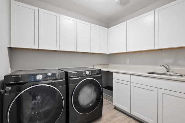 laundry area featuring a textured ceiling, a sink, washer and dryer, cabinet space, and light wood finished floors