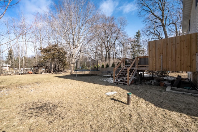 view of yard featuring a deck, stairway, a trampoline, and fence