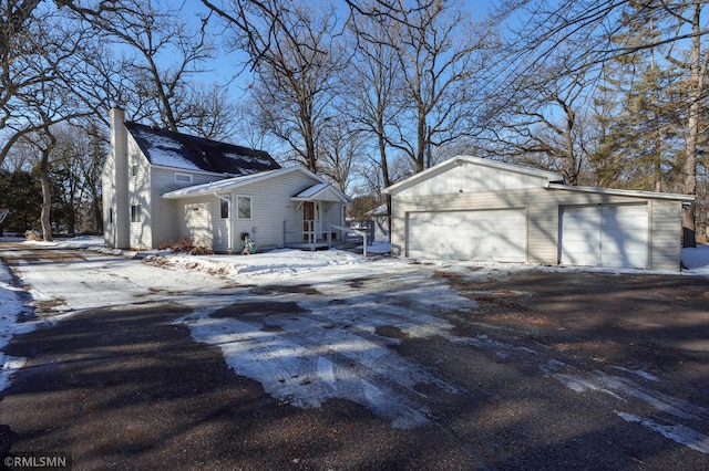 view of snowy exterior with an outbuilding, a chimney, and a garage