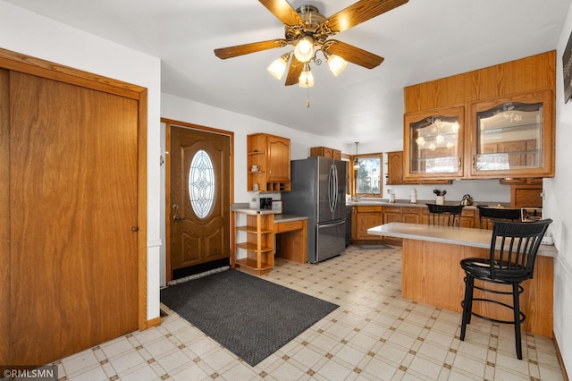 kitchen with brown cabinets, light floors, open shelves, freestanding refrigerator, and a peninsula