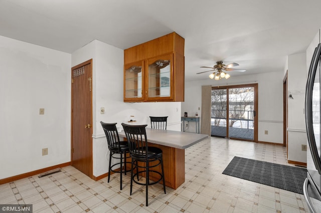 kitchen featuring a peninsula, baseboards, brown cabinets, light floors, and glass insert cabinets