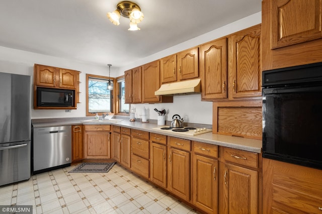 kitchen with brown cabinetry, light floors, under cabinet range hood, black appliances, and a sink