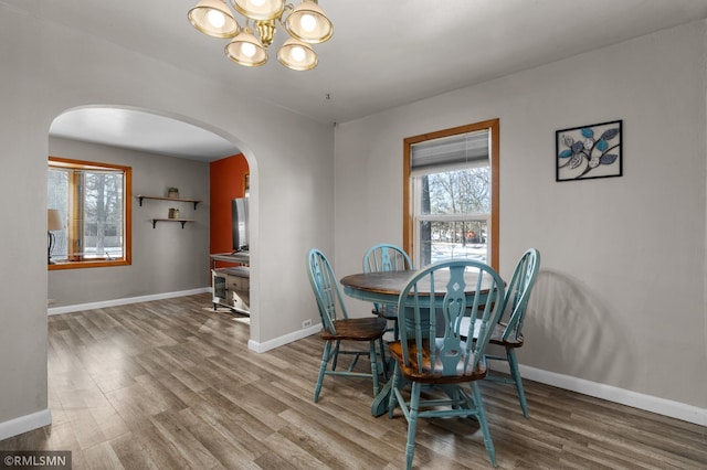 dining area featuring arched walkways, a notable chandelier, wood finished floors, and baseboards