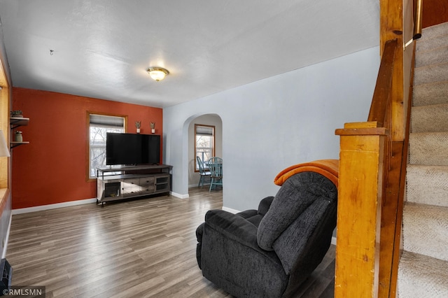 living area featuring stairway, baseboards, arched walkways, and wood finished floors