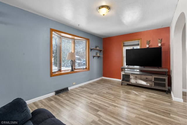 living room with arched walkways, visible vents, baseboards, and wood finished floors