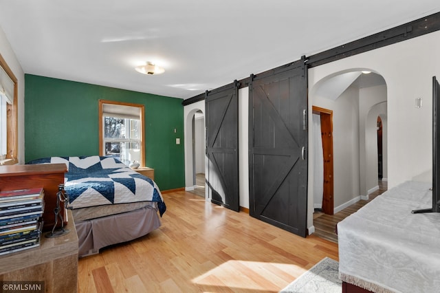 bedroom with arched walkways, a barn door, light wood-type flooring, and baseboards