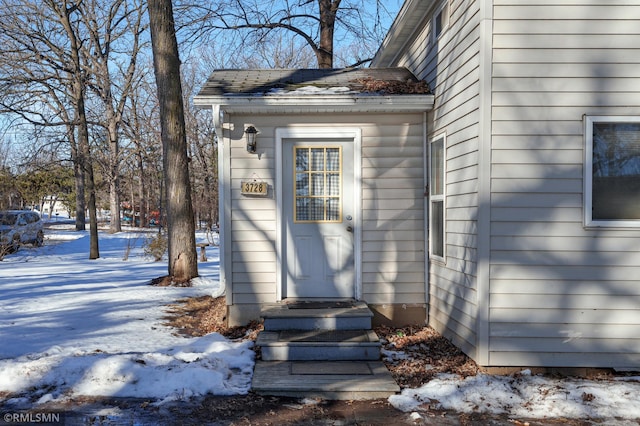 snow covered property entrance featuring roof with shingles