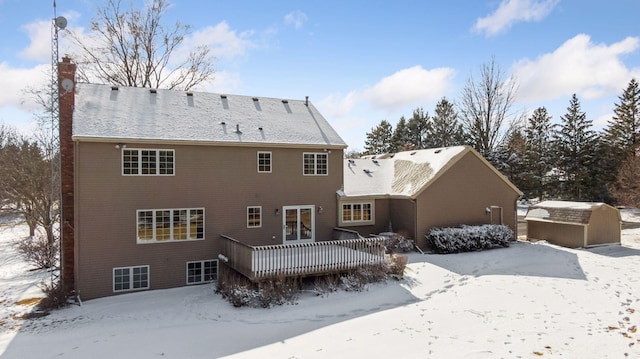 snow covered rear of property featuring a wooden deck and a chimney