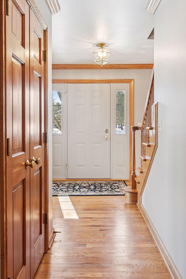 entryway with stairs, baseboards, light wood-type flooring, and ornamental molding