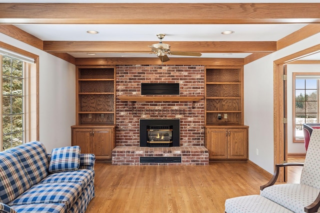 living area featuring beamed ceiling, built in shelves, a fireplace, and light wood finished floors