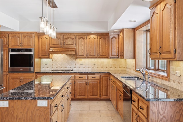 kitchen featuring dark stone countertops, brown cabinetry, custom exhaust hood, a sink, and appliances with stainless steel finishes