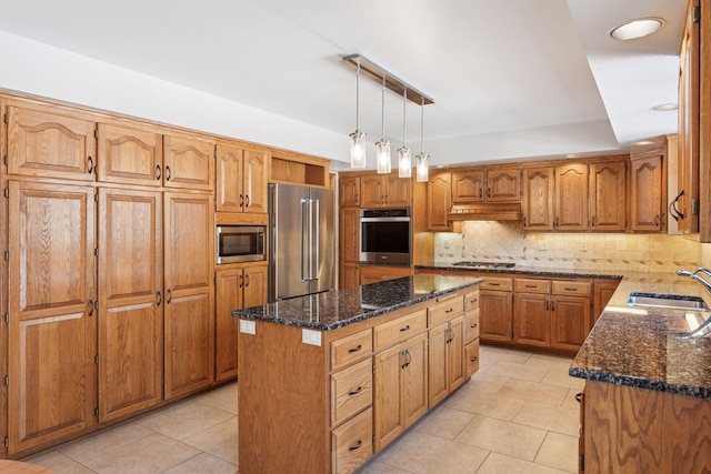 kitchen featuring dark stone counters, a sink, stainless steel appliances, tasteful backsplash, and a center island