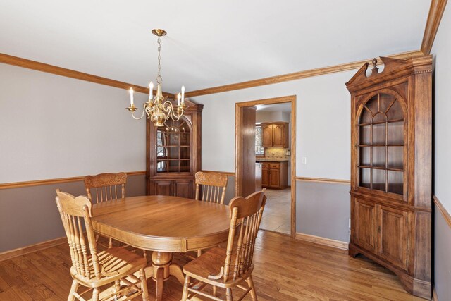 dining space featuring a notable chandelier, baseboards, light wood-style floors, and ornamental molding