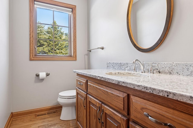 half bathroom with visible vents, toilet, wood finished floors, baseboards, and vanity