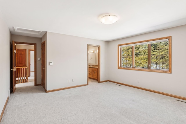 unfurnished bedroom featuring visible vents, baseboards, light colored carpet, attic access, and ensuite bath