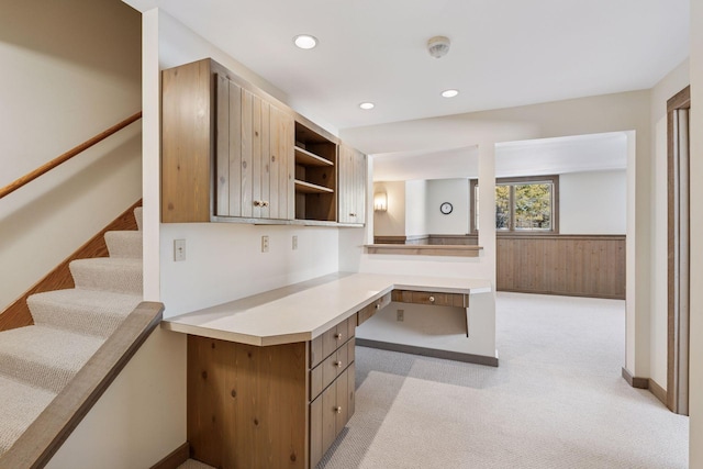 kitchen featuring wooden walls, a wainscoted wall, built in study area, a peninsula, and light carpet