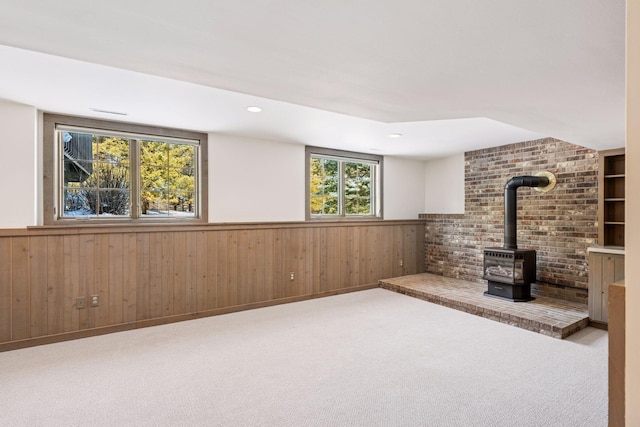 below grade area with wooden walls, wainscoting, a wood stove, and carpet floors