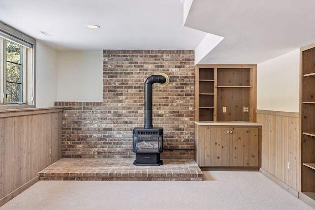 unfurnished living room with wainscoting, carpet flooring, wood walls, and a wood stove