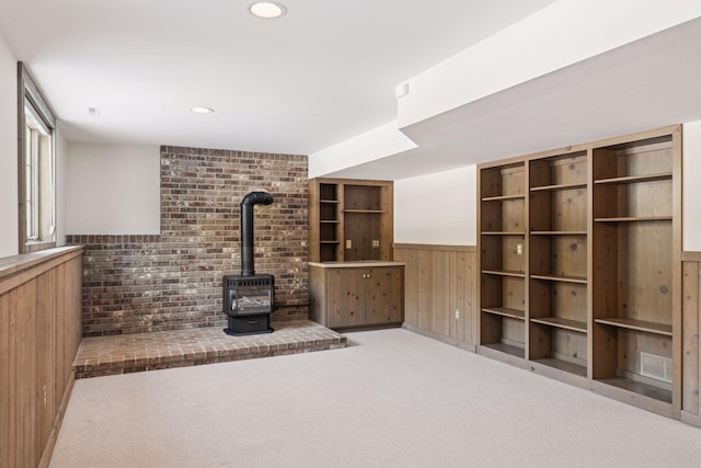 unfurnished living room with a wood stove, recessed lighting, wood walls, wainscoting, and carpet flooring