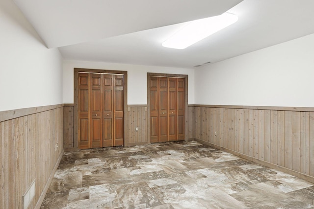 unfurnished bedroom featuring a wainscoted wall, multiple closets, and wooden walls