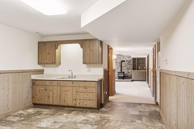 kitchen featuring wooden walls, a wainscoted wall, light countertops, a wood stove, and a sink