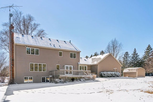 snow covered property with a wooden deck, an outbuilding, a storage shed, and a chimney