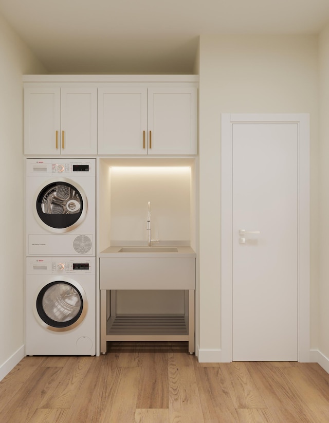 washroom with cabinet space, baseboards, stacked washer / dryer, light wood-style flooring, and a sink