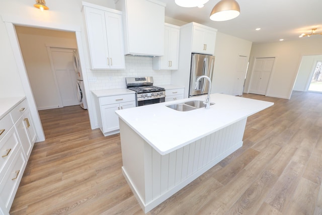 kitchen with decorative backsplash, a sink, light wood-style floors, stainless steel appliances, and an island with sink